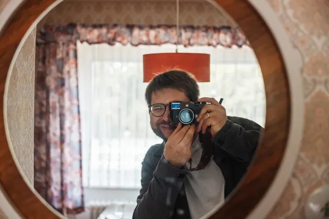 Till Heidrich fotografiert sich selbst in einem runden Spiegel, die Kamera vor dem Gesicht.